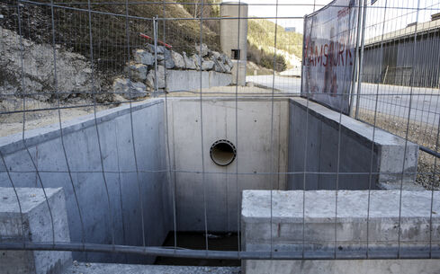 Auf dem Bild ist ein vertieftes, von hellem Kies und Schotter eingefasste Wasseransammlung mit zwei Betonbauten am oberen und unteren Ende zu sehen.