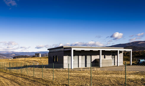 The picture shows an elongated, flat building in an open terrain with three entrances to the complex.