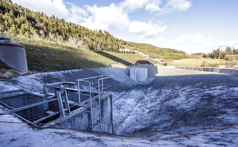 The picture shows a deepened accumulation of water, surrounded by light shingle and gravel, with two concrete structures at the top and bottom.