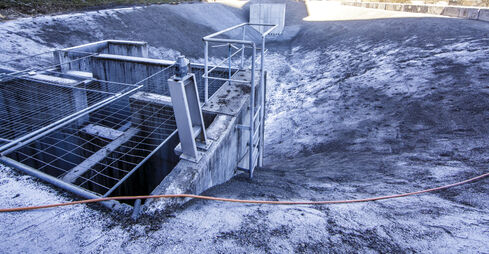 The picture shows a deepened accumulation of water, surrounded by light shingle and gravel, with two concrete structures at the top and bottom.