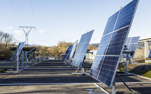 Nell'immagine si vedono recipienti per l'acqua disposti verticalmente nel terreno, con moduli fotovoltaici fissati ad una parete sulla destra.