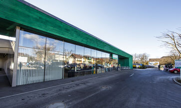 The picture shows the entrance portal, framed by a green structure with a long glass front.