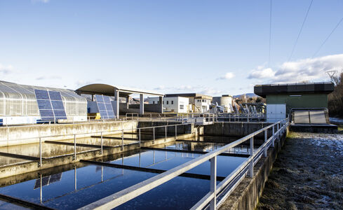 Nell'immagine si vedono recipienti per l'acqua disposti verticalmente nel terreno, con moduli fotovoltaici fissati ad una parete sulla destra.