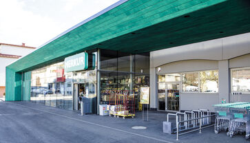 The picture shows the entrance portal, framed by a green structure with a long glass front.