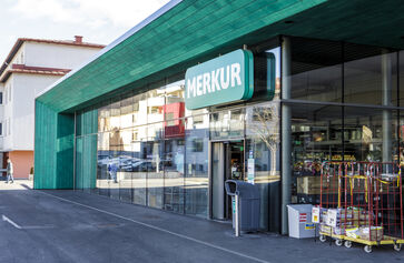 The picture shows the entrance portal, framed by a green structure with a long glass front.